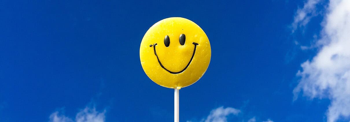 Yellow Smiley face on a stick against a blue sky with some clouds