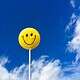 Yellow Smiley face on a stick against a blue sky with some clouds
