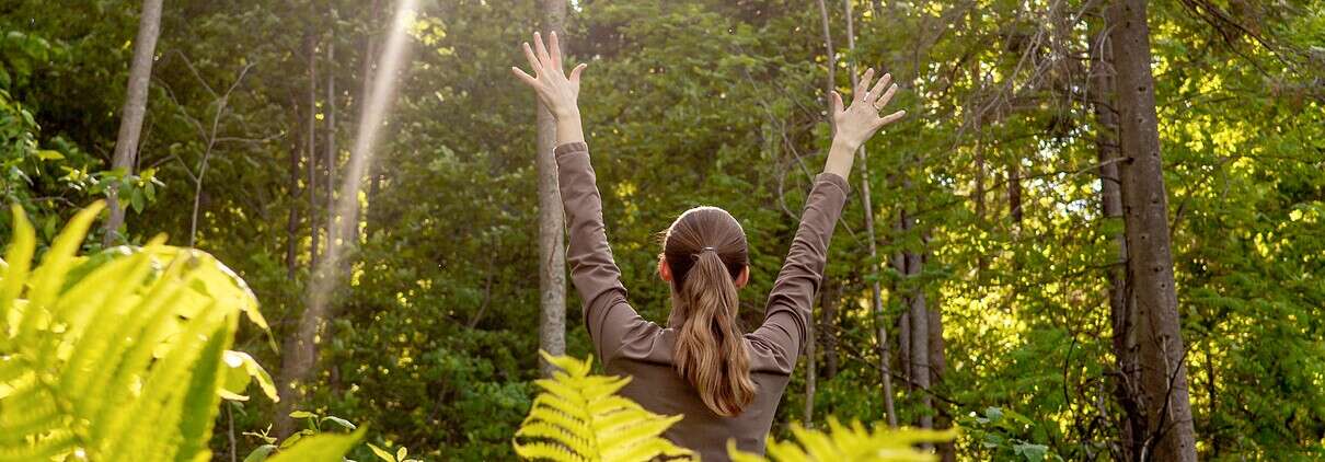 Woman in the forest with facing backwards with arms up in the sky - hope concept