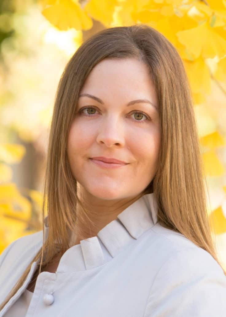 Beautiful woman with long brown hair smiling outdoors in autumn, promoting mental health and counseling services.