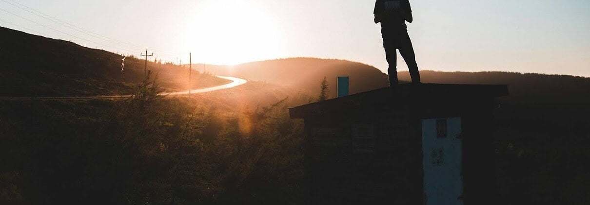 Silhouette of a person standing on a roof at sunset with mountains in the background.