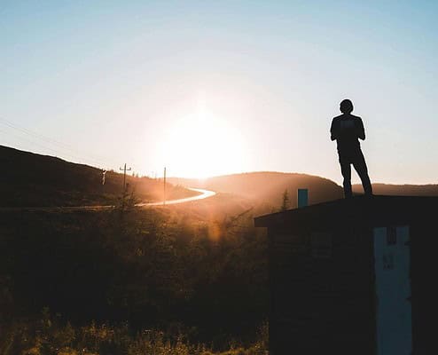 Silhouette of a person standing on a roof at sunset with mountains in the background.