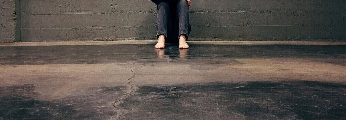 Lonely person sitting against cracked concrete wall feeling distressed or overwhelmed.