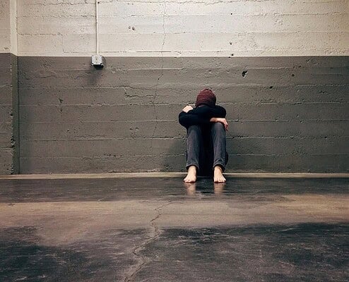 Lonely person sitting against cracked concrete wall feeling distressed or overwhelmed.