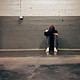 Lonely person sitting against cracked concrete wall feeling distressed or overwhelmed.
