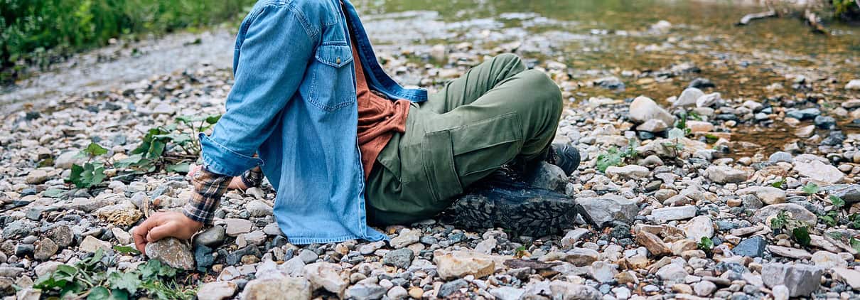 Relaxed man sitting by a creek in nature, highlighting mental health and outdoor therapy.