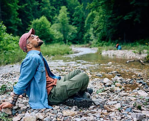 Relaxed man sitting by a creek in nature, highlighting mental health and outdoor therapy.