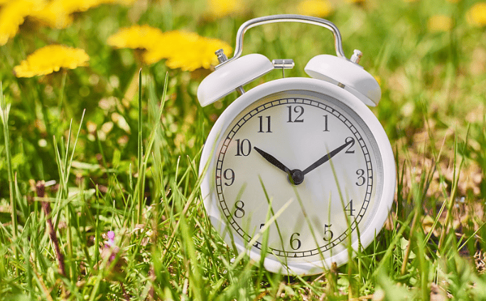 White alarm clock in grass, symbolizing time management challenges with ADHD.