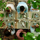 Overhead view of people seated around a long wooden table enjoying an outdoor meal surrounded by greenery, with candles, place settings, and shared dishes arranged for a communal dining experience.