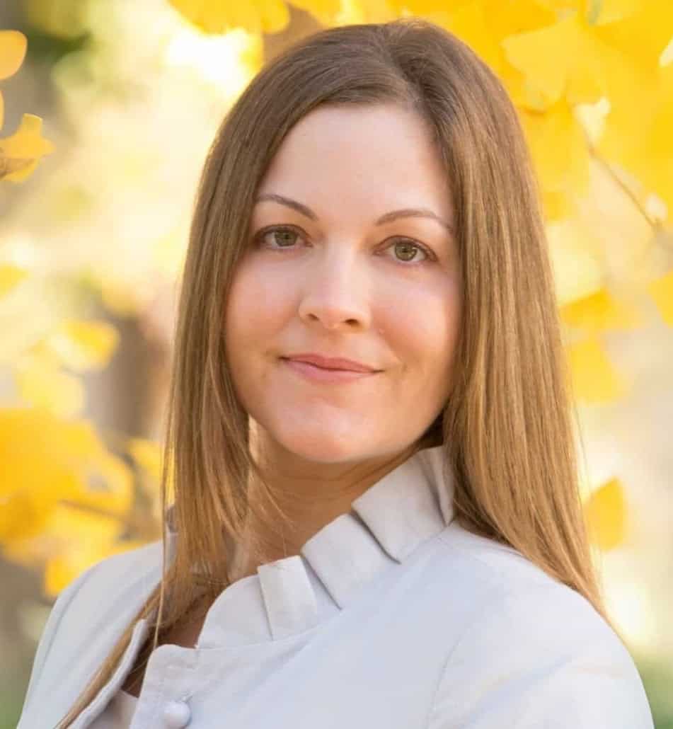 Woman smiling outdoors with yellow autumn leaves in background.